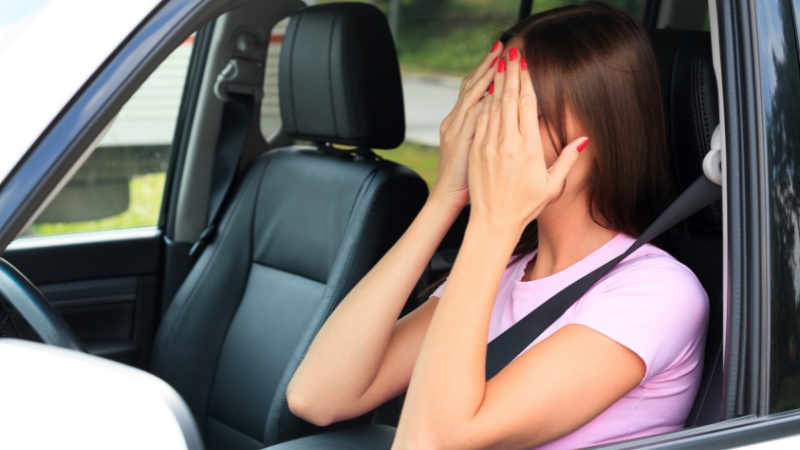 A woman sits in her car with her hands covering her face, capturing a quiet moment of burnout that shows rest can start anywhere